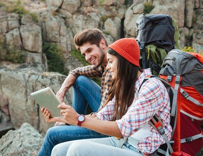 Ein Mann und eine Frau sitzen in den Bergen und schauen auf ein Tablet. Foto: Colourbox